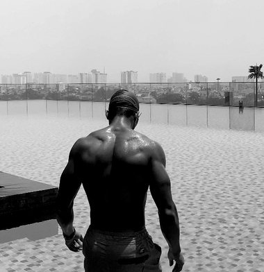 Back view of a muscular figure standing beside an infinity pool.